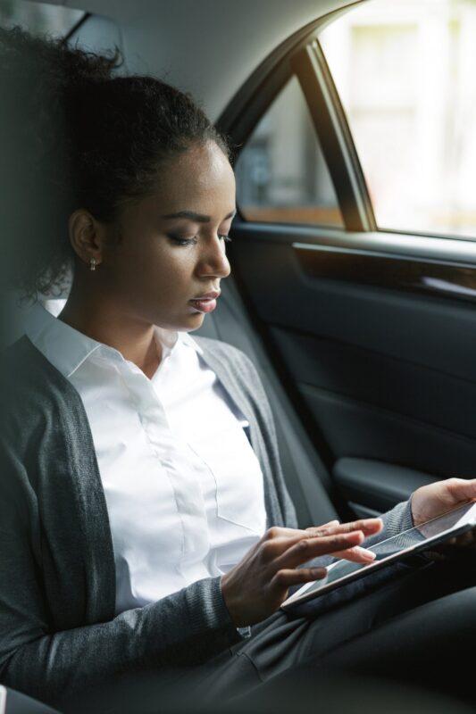 Businesswoman typing on digital tablet in back seat of a car